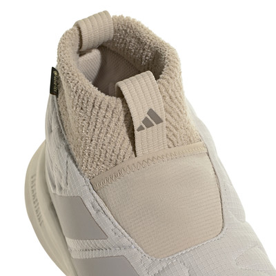 Egy bézs Adidas cipő felső részének részlete, textil felülettel és logóval.