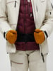 Person in beiger Jacke mit weinroter Weste und Handschuhen.