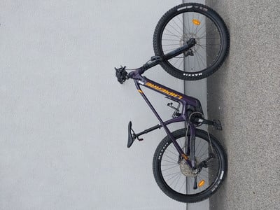 Lila Mountainbike mit schwarzen Rädern, das an einer Wand lehnt.