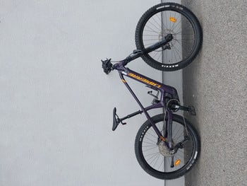 Lila Mountainbike mit schwarzen Rädern, das an einer Wand lehnt.