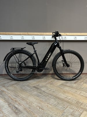 Ein schwarzes Cube E-Bike steht auf einem Holzboden vor einer grauen Wand.