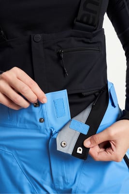 Detail modrých lyžařských kalhot s černou náprsenkou a zapínáním na druk. Detail modrých lyžařských kalhot s černou náprsenkou a zapínáním na druk.