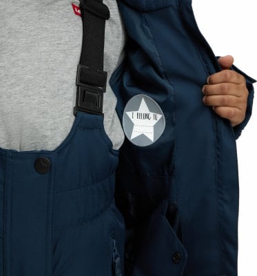 Detail einer Jacke mit eingenähtem Etikett 'I BELONG TO' und Teil einer Skihose. Detail einer Jacke mit eingenähtem Etikett 'I BELONG TO' und Teil einer Skihose.