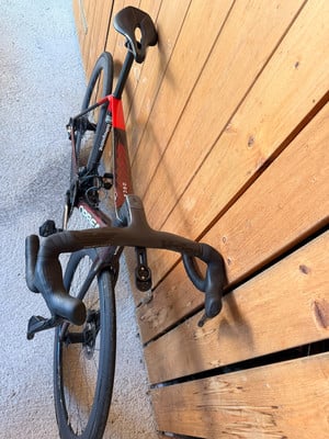 Ein Rennrad mit rotem Rahmen, das an einer Holzwand lehnt.