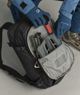 Eine Person packt einen Helm und Skistöcke in einen Rucksack. Eine Person packt einen Helm und Skistöcke in einen Rucksack.