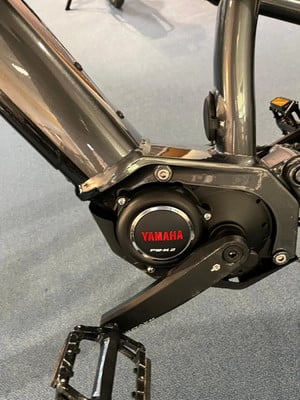 Nahaufnahme eines E-Bikes mit Yamaha-Logo und Kurbel auf grauem Teppich. Nahaufnahme eines E-Bikes mit Yamaha-Logo und Kurbel auf grauem Teppich.