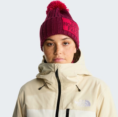Mädchen in einer beige Jacke und einer weinroten Bommelmütze mit Logo. Mädchen in einer beige Jacke und einer weinroten Bommelmütze mit Logo.