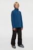 Junge in blauem Fleece-Pullover und schwarzer Skihose mit Skischuhen.