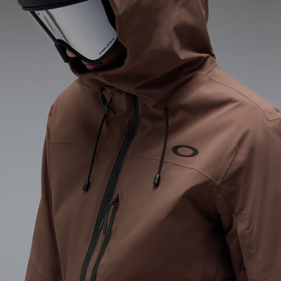 Ein Mann in einer braunen Oakley-Jacke und Skibrille blickt nach unten.