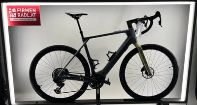 Ein graues E-Bike mit gelber Gabel steht auf einem Ständer vor einer weißen Wand. Ein graues E-Bike mit gelber Gabel steht auf einem Ständer vor einer weißen Wand.