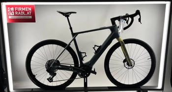 Ein graues E-Bike mit gelber Gabel steht auf einem Ständer vor einer weißen Wand.