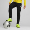 Ein Mann in schwarzer Hose und gelben Fußballschuhen steht mit einem Ball.