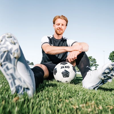 Ein Fußballer sitzt mit einem Ball und Fußballschuhen auf dem Rasen. Ein Fußballer sitzt mit einem Ball und Fußballschuhen auf dem Rasen.