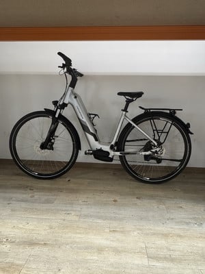 Modernes silbernes E-Bike mit Schutzblechen und Gepäckträger, drinnen abgestellt. Modernes silbernes E-Bike mit Schutzblechen und Gepäckträger, drinnen abgestellt.