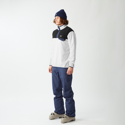 Ein Mann in einer blauen Mütze, einem weiß-schwarzen Fleece-Pullover und blauen Skihosen.
