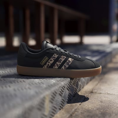 Fekete Adidas sneakerek leopárdmintás csíkokkal és gumitalppal lépcsőkön.