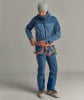 Ein Mann in blauer Jacke und Hose mit Klettergurt passt seine Ausrüstung an.