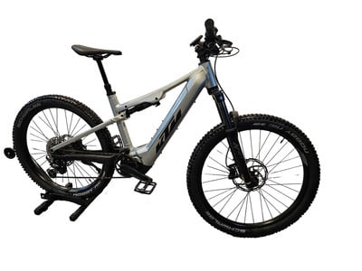 Ein silbernes KTM Mountain E-Bike mit Federung und schwarzen Rädern.