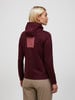 Rückansicht einer Frau in einem burgunderroten Kapuzenpullover und beiger Hose.