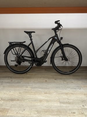 Schwarzes KTM E-Bike mit Schutzblechen und Gepäckträger auf Holzboden. Schwarzes KTM E-Bike mit Schutzblechen und Gepäckträger auf Holzboden.