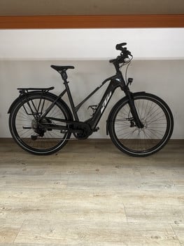 Schwarzes KTM E-Bike mit Schutzblechen und Gepäckträger auf Holzboden.