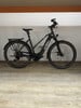 Schwarzes KTM E-Bike mit Schutzblechen und Gepäckträger auf Holzboden.