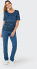 Eine Frau in einem blauen bedruckten T-Shirt und blauen Hosen steht.