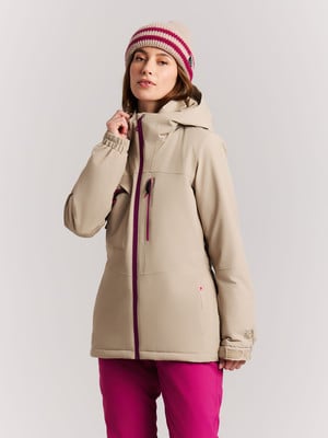 Eine Frau in einer beigen Jacke und pinker Hose mit Mütze auf dem Kopf.
