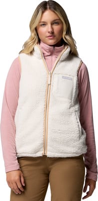 Eine Frau in einer cremefarbenen Fleeceweste mit pinkem Rollkragenpullover und brauner Hose.