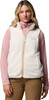 Eine Frau in einer cremefarbenen Fleeceweste mit pinkem Rollkragenpullover und brauner Hose.