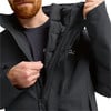 Ein Mann schließt eine schwarze Winterjacke mit Kapuze und gestepptem Futter.