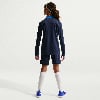 Ein Mädchen in einem dunkelblauen Fußballtrikot mit weißem Streifen und blauen Shorts.