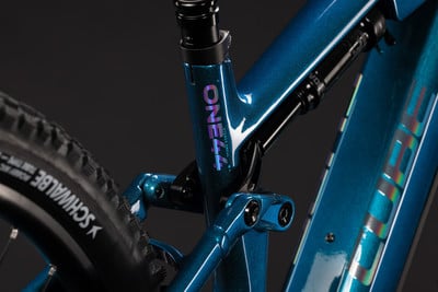 Detail des hinteren Teils eines blauen E-Mountainbikes mit Dämpfer und Logo. Detail des hinteren Teils eines blauen E-Mountainbikes mit Dämpfer und Logo.