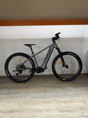 Graues E-Mountainbike mit schwarzen Rädern und gelben Details. Graues E-Mountainbike mit schwarzen Rädern und gelben Details.