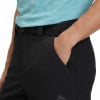 Ein Mann steckt seine Hand in die Tasche einer schwarzen Hose mit einem blauen Hemd.