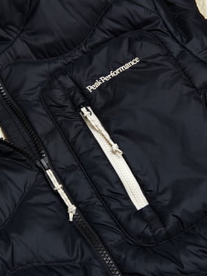 Detail einer schwarzen Daunenjacke mit Peak Performance Logo und Reißverschluss. Detail einer schwarzen Daunenjacke mit Peak Performance Logo und Reißverschluss.