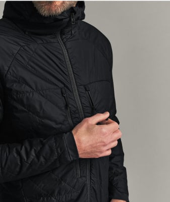 Ein Mann in einer schwarzen gesteppten Kapuzenjacke hält den Reißverschluss der Jacke.