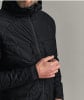 Ein Mann in einer schwarzen gesteppten Kapuzenjacke hält den Reißverschluss der Jacke.