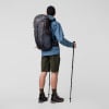 Mann in blauer Jacke und Shorts mit Rucksack und Wanderstöcken.