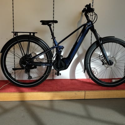 Ein blaues Conway E-Bike mit Gepäckträger und Federung in Innenräumen. Ein blaues Conway E-Bike mit Gepäckträger und Federung in Innenräumen.
