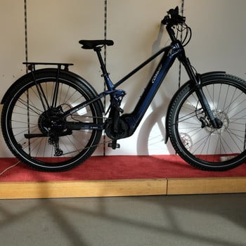 Ein blaues Conway E-Bike mit Gepäckträger und Federung in Innenräumen.