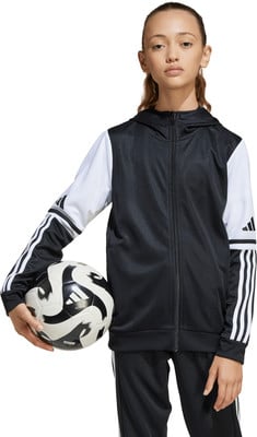 Ein Mädchen mit einem Ball in der Hand in einer schwarz-weißen Jacke vor weißem Hintergrund.