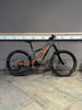 Graues KTM E-Bike mit orangefarbenen Details steht auf Holzboden.