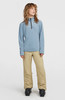 Ein Mädchen in einem blauen Fleece-Pullover und einer beige Skihose steht vor weißem Hintergrund.