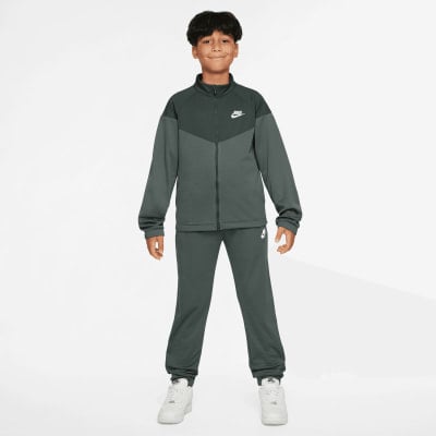Junge im dunkelgrauen Nike Trainingsanzug mit Logo auf Brust und Bein.