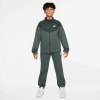Junge im dunkelgrauen Nike Trainingsanzug mit Logo auf Brust und Bein.