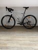 Ein graues Gravelbike mit schwarzen Rädern und Lenker steht auf einem Holzboden.