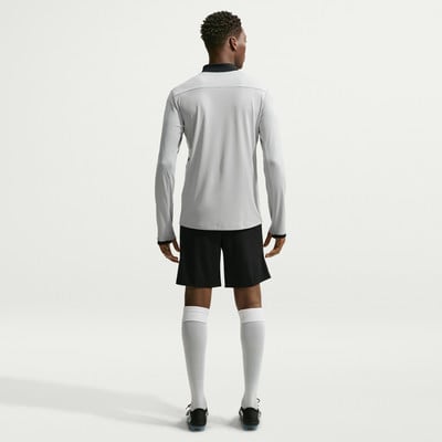 Ein Mann in einem langen grauen Hemd und schwarzen Shorts mit weißen Socken.