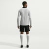 Ein Mann in einem langen grauen Hemd und schwarzen Shorts mit weißen Socken.