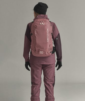Rückansicht einer Person mit rosafarbenem Rucksack und Skibekleidung.